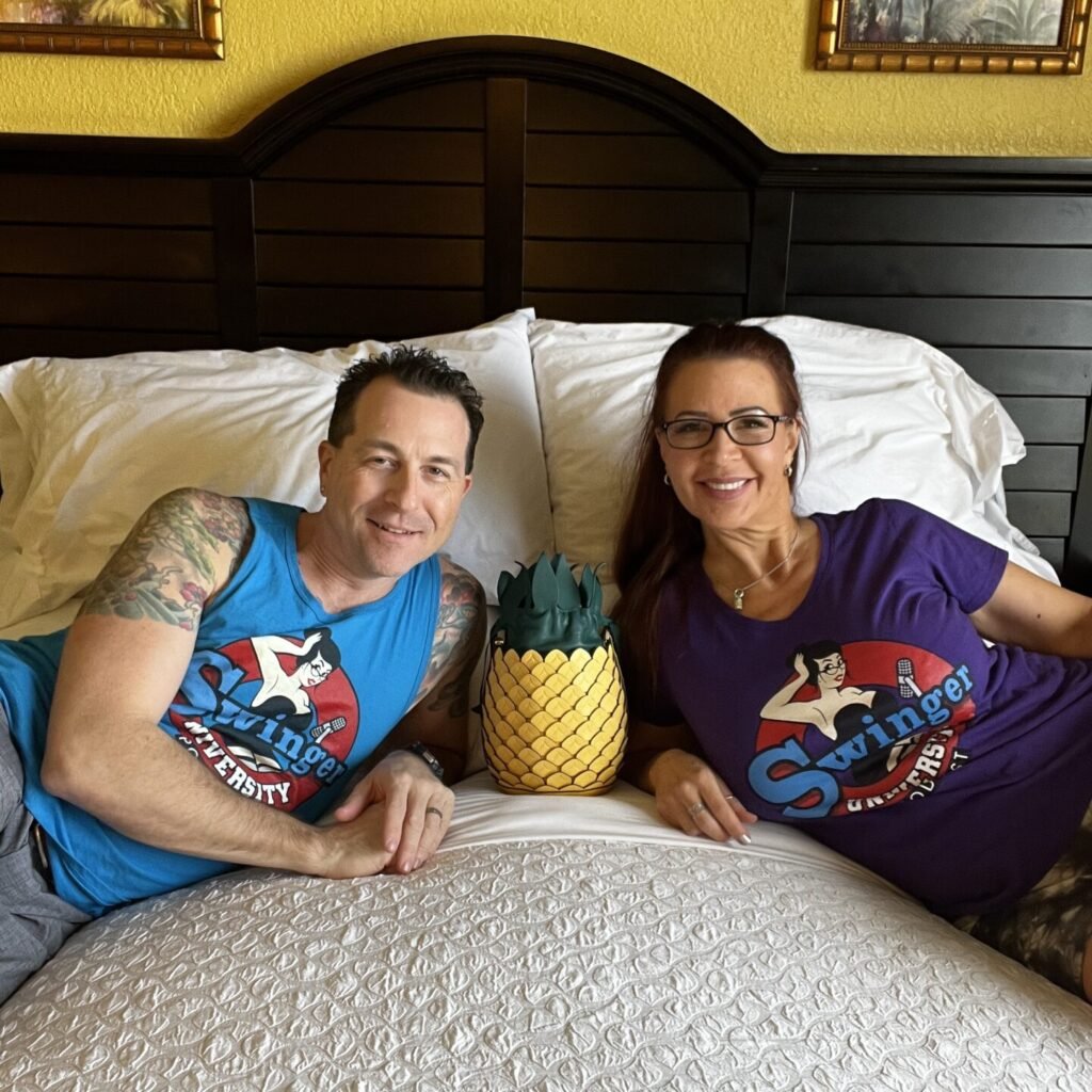 Ed and Phoebe on a bed with pineapple purse from Kate Spade