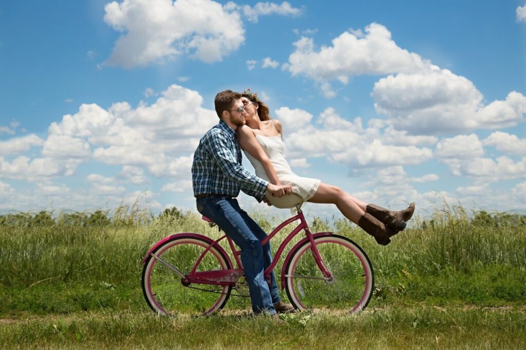 man and woman riding a bike through a field on a cloudy day