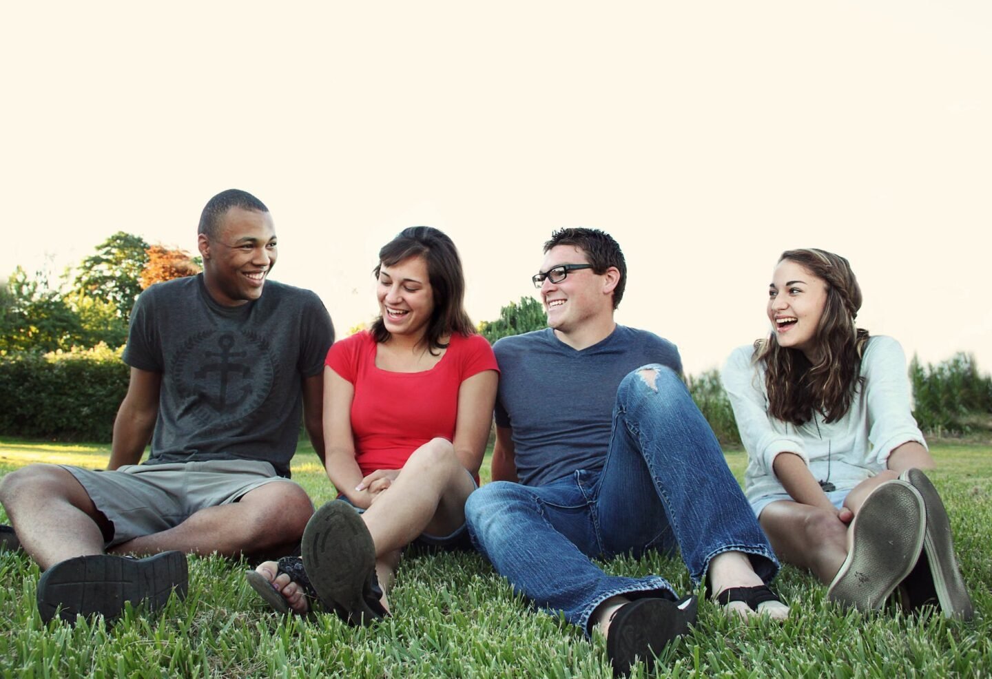 smiling women and men sitting on green grass after meeting through their dating profile